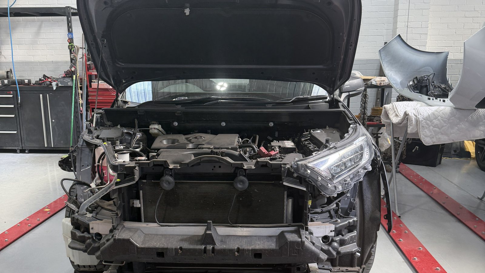 A car on the chassis alignment jig in the Fineline workshop, bonnet up and front stripped for repair