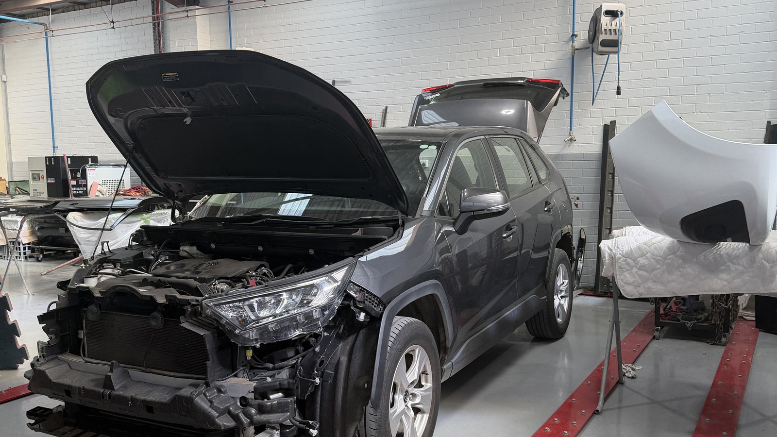 A car in the Fineline workshop with the bonnet up and the front stripped, the damage laid open for assessment